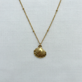 Gold shell pendant with symmetrical bead details on white linen