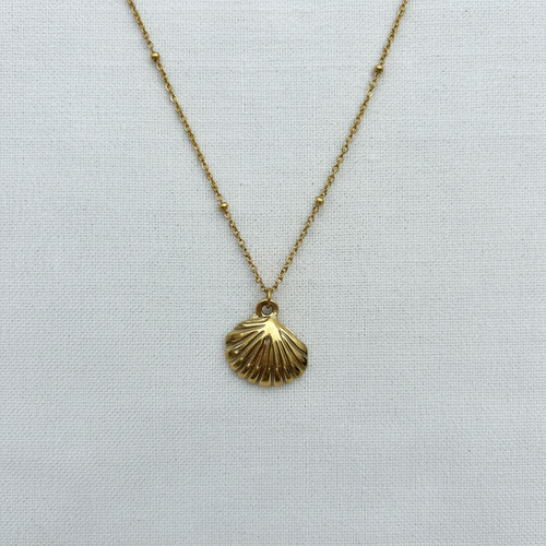 Gold shell pendant with symmetrical bead details on white linen